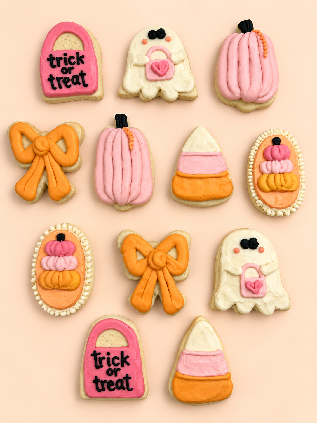 A set of Halloween-themed sugar cookies decorated with pink, orange, and white icing, arranged on a solid pale pink background. The cookies include jack-o'-lantern, candy corn, ghost, and lock-shaped designs with 'trick or treat' written on two of them.